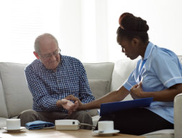 A nurse and an elderly man are seated together on a couch