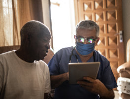 A doctor and an elderly man seated in a chair, both focused on a tablet