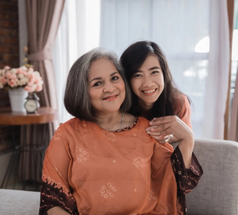 A female hugging the senior woman sitting on a sofa